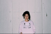 a woman in a pink sweatshirt posing against a wall